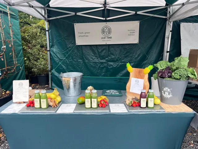 The Leaf TRNR market stall with bottled smoothies, fresh fruit and leafy greens beneath a green canopy.